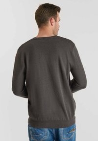 Mörkgrå tröja med rund hals, långa ärmar och ribbat avslut, som matchas med blå denimjeans. Mjuk tyg, enkel design, inga synliga mönster eller logotyper.