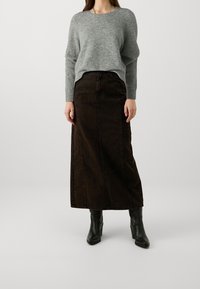 Pull gris en tricot avec un col arrondi, associé à une jupe en denim marron foncé longue jusqu'au sol. La tenue est complétée par des bottes à talons noires.