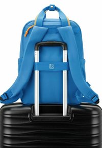 Zaino blu con spallacci regolabili, dotato di un cursore arancione, posizionato su una valigia nera rigida con superficie testurizzata.