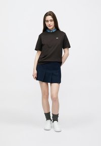 Black cotton t-shirt with a logo, paired with a navy pleated skirt. White sneakers and green ribbed socks complete the outfit.