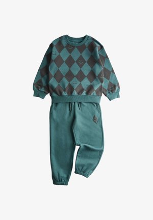 Bluza z zielonym i ciemnoszarym wzorem w romby z małymi uśmiechniętymi buźkami, zestawiona z zielonymi spodniami z elastyczną talią i ściągaczami oraz małą naszywką w romby.