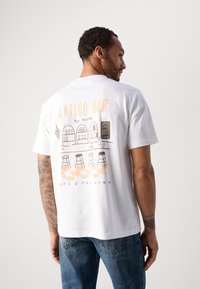 Witte katoenen T-shirt met een grafische illustratie van een bar scène met stoelen en drankjes, accenten van oranje en zwarte tekst op de achterkant.