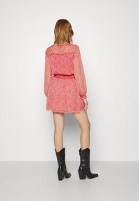 Robe rose à motif floral avec manches longues en tissu transparent et taille cintrée, assortie à des bottes de cowboy noires à talon évasé.