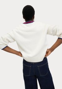 Maglione bianco con orlo e polsini a costine, caratterizzato da un collo a righe multicolore. Abbinato a jeans in denim blu scuro.