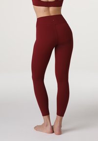 Leggings bordeaux a vita alta realizzati in tessuto elasticizzato, caratterizzati da una texture liscia e un design aderente. Le cuciture piatte offrono comfort.