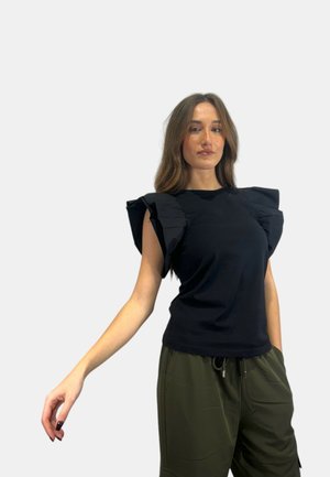 Top nero con maniche a volant, design aderente e tessuto morbido. Abbinato a pantaloni verde oliva larghi, con vita regolabile.