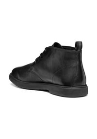 Botas de cuero negras hasta el tobillo con una textura suave, puntera redondeada y suela de goma plana. Presentan una lengüeta en la parte posterior para facilitar su puesta.