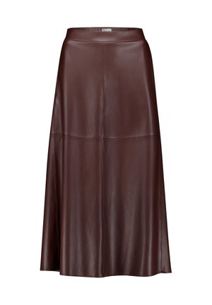 Femme portant un pull boutonné marron foncé duveteux, une longue jupe en cuir assortie et des bottes noires à talons, debout devant un fond uni.