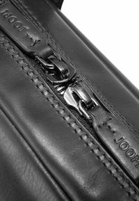 Schwarze Lederhandtasche mit silbernem Reißverschluss mit zwei Zippern, geprägtem Logo und feiner Naht entlang der Kanten.