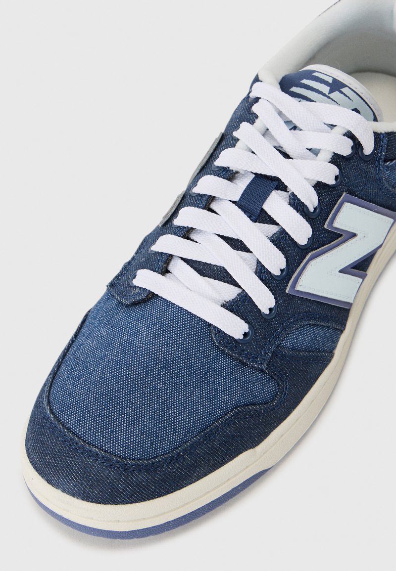 Denim sneakers in dark blue with white laces, round toe, padded collar, and a light blue logo accent on the side.