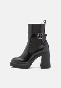 Schwarze Knöchelstiefel mit glänzender Lederoberfläche, elastischen seitlichen Einsätzen, breitem Blockabsatz und dekorativer Schnalle auf dem Blatt.