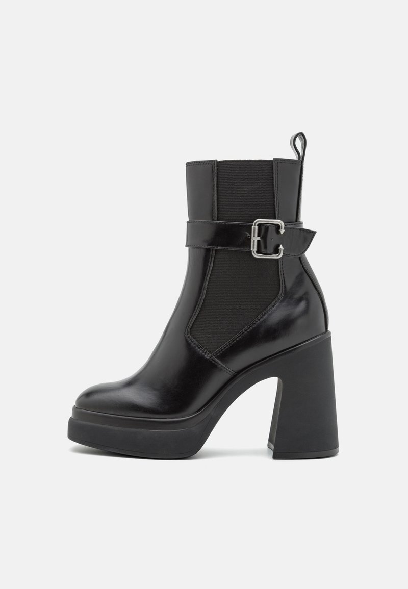 Schwarze Knöchelstiefel mit glänzender Lederoberfläche, elastischen seitlichen Einsätzen, breitem Blockabsatz und dekorativer Schnalle auf dem Blatt.