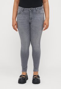 Szürke skinny farmernadrág sima denim textúrával, elülső zsebekkel és normál derékkal. Masszív fekete lábbelivel párosítva.