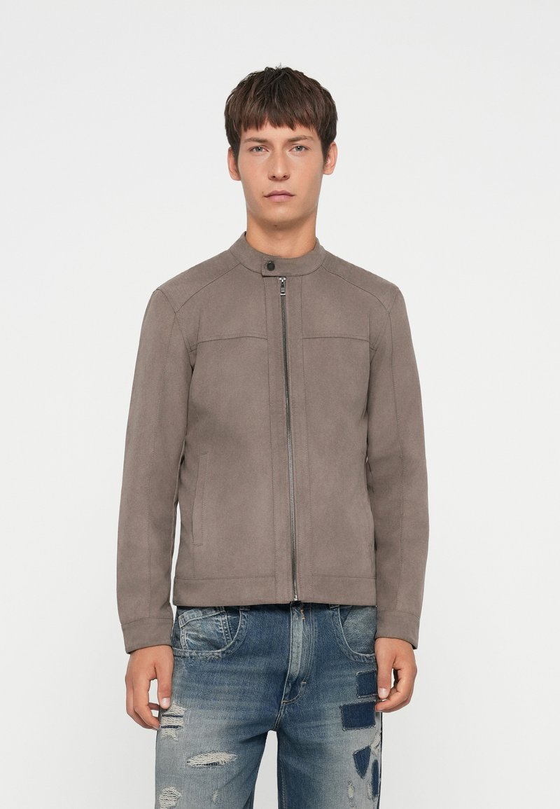 Chaqueta gris con cremallera, de cuello alto, fabricada con tejido suave. Presenta dos bolsillos laterales y un diseño aerodinámico con costuras mínimas.
