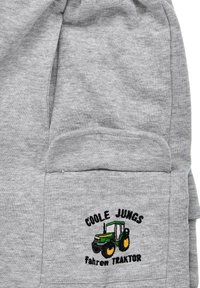Grauer Sweatshirtstoff mit einer Fronttasche. Verziert mit schwarzem und buntem Traktor-Stickerei sowie dem Text "COOLE JUNGS fahren TRAKTOR."