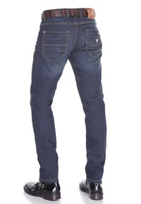 Donkerblauwe denim slim-fit jeans met subtiele gele stiksels, voorzien van vijf zakken en een bruine riem met zilveren studs.