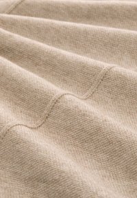 Beige strukturierter Stoff mit feinem Strickmuster, das weiche Falten und sanfte Schatten auf der Oberfläche bildet.