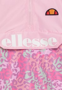 Jasnoróżowy wiatrówka z białym logo "ellesse", z kołnierzem na zamek błyskawiczny i wzorem w panterkę w jasnym różu, purpurze i miętowej zieleni.