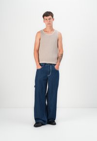 Top de tirantes de canalé beige claro combinado con unos jeans anchos de rayas azules. Los jeans tienen un ajuste holgado y bolsillos laterales, complementados con zapatos negros.