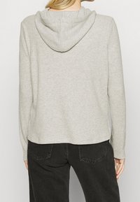Hellgraue gerippte Kapuzenjacke mit einer vorderen Tasche, seitlichen Schlitzen und lässiger Passform. Sie verfügt über eine Kapuze mit Kordelzug und lange Ärmel.
