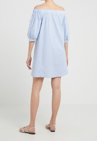 Modrá a bílá pruhovaná šaty s odhalenými rameny, s nafouknutými rukávy, elastickými manžetami a uvolněným střihem, doplněné o ploché sandály.