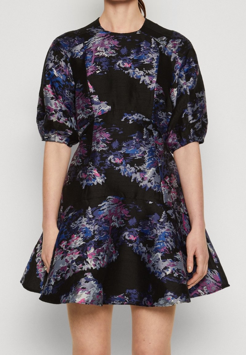 Blommig klänning med svart bas, med mönster i lila, blå och rosa. Puffärmar och en utsvängd kjol skapar en strukturerad silhuett.