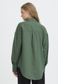Grünes, vertikal gestreiftes Hemd mit lockerer Passform, langen Ärmeln, Knopfmanschetten und abgerundetem Saum, aus einem leichten Stoff gefertigt.