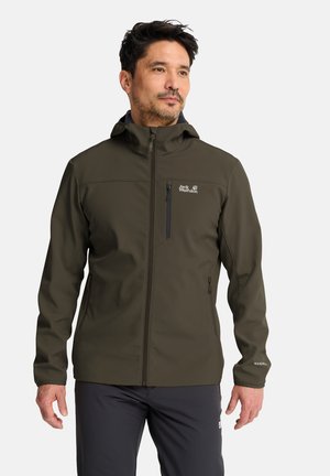 Man draagt een olijfgroene outdoor jas met capuchon, met ritsen op de borst en zijkanten, staand tegen een effen achtergrond.