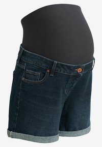Shorts de maternidad de mezclilla con un lavado azul oscuro, que cuentan con un panel elástico negro para la pancita, dobladillos enrollados y detalles de herrajes en color cobre.