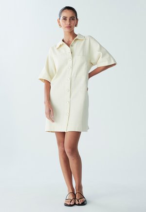 Kurzärmliges, hellgelbes Hemdkleid mit Kragen und einer Vordertasche, aus strukturiertem Stoff gefertigt und mit geradem Saum.