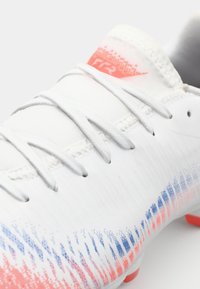 White soccer cleat with a textured design, featuring a gradient of blue and pink accents. Includes gray laces and a padded collar.