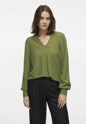 Haut vert texturé avec un col en V et des manches longues, présentant un motif de vagues ; associé à un pantalon noir à jambes larges.