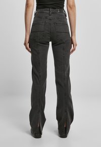 Jeans de mezclilla negra de pierna ancha con dobladillos partidos, dos bolsillos traseros y costuras visibles. Cintura alta y textura suave.