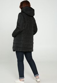 Musta toppatakki hupulla, jossa on tikattu kuviointi ja keskipitkä leikkaus. Suunniteltu sivutaskuilla ja kiiltävällä, sileällä kankaalla.