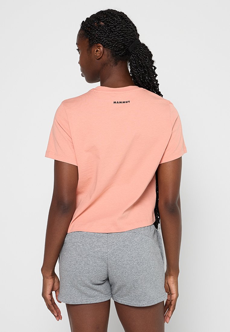 Krótki rękawek, skrojony t-shirt w kolorze brzoskwiniowym z czarnym logo "Mammut" na plecach, w połączeniu z szarymi szortami. Bawełnowy materiał, luźny krój.