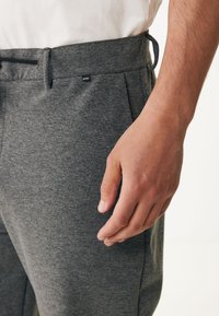 Grijze joggingsbroek van een gestructureerde stof, met een elastische tailleband en trekkoorden. Heeft zijzakken en een klein merkembleem bij de taille.
