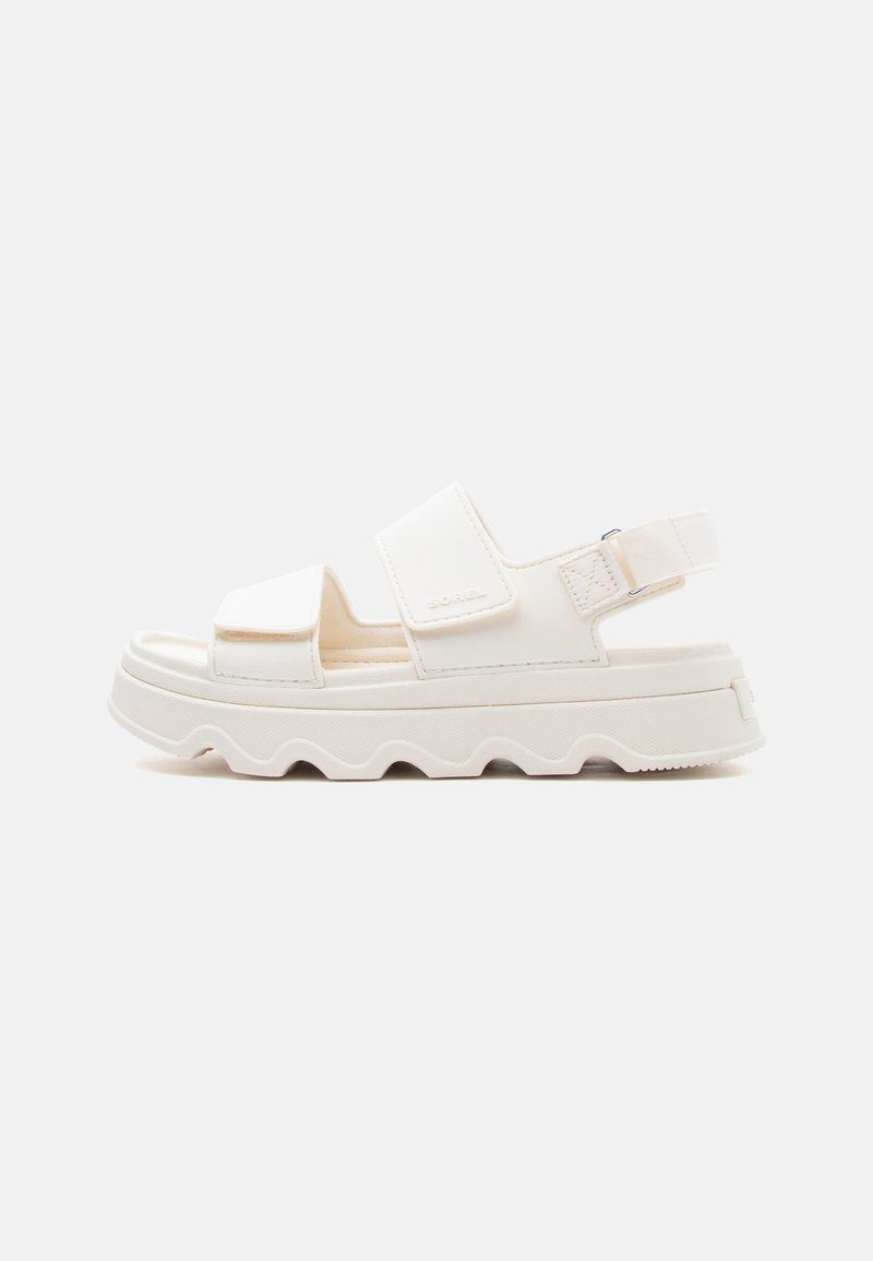 Λευκό δίπατο σανδάλι με δύο ρυθμιζόμενα λουράκια και αγκράφα σε κυματιστή υφή σόλας, εμφανιζόμενο από το πλάι σε απλό φόντο.