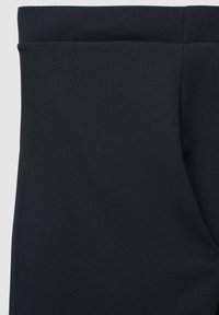 Primo piano di un tessuto nero con una tasca laterale e una cucitura in vita, che mostra la texture e i dettagli della costruzione del capo.