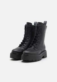 Bottes de combat en cuir noir avec semelles épaisses, lacets hauts et quincaillerie durable. Présente des languettes de talon marquées et une texture lisse.