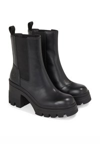 Botas negras de cuero hasta el tobillo con paneles laterales elásticos, suelas de goma gruesas y un ligero tacón. Presentan un acabado texturizado y lengüetas para facilitar el calce.