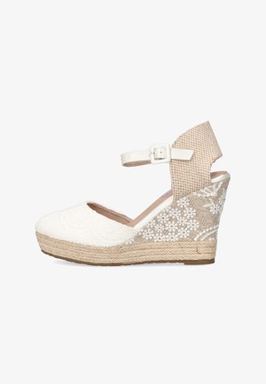 Cuña de espadrille blanca con parte superior texturizada y detalles de encaje floral. Presenta una correa de tobillo tejida en beige y una plataforma envuelta en yute.