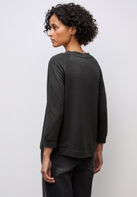 Tummanharmaa pitkähihainen paita, jossa on pyöreä kaula-aukko ja raglan-hihat. Valmistettu pehmeästä kankaasta, jossa on rento malli ja minimaliset ompeluyksityiskohdat.