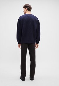 Tengerészkék kötött pulóver laza szabással, kerek nyakkivágással és finom textúrával, fekete szabott nadrággal és fekete cipővel párosítva.