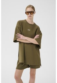 Olijfgroen oversized t-shirt met een ronde hals en korte mouwen, gecombineerd met bijpassende shorts. Inclusief geborduurd logo detail.