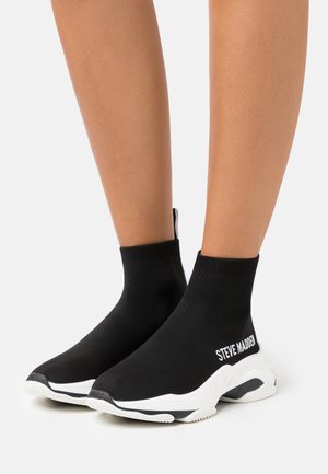 Black sock-style sneakers with elastic upper, white sole, and textured black toe cap. Features "STEVE MADDEN" logo on the side.