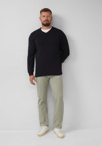Marineblauer V-Ausschnitt-Pullover, hellgrüne Chinos und weiße Sneakers. Einfaches Design, glattes Material und lässige Passform.
