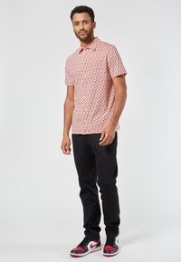 Rood-wit gestippeld shirt met korte mouwen en geknoopte kraag, gecombineerd met zwarte tapered broek en rood-zwart sneakers.