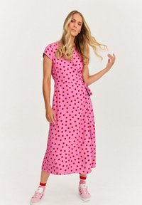 Růžové zábalové šaty s červenými puntíky, krátké rukávy a zavazování v pase. Spárováno s růžovými teniskami a červenými ponožkami.