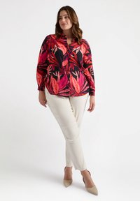 Blusa de manga larga con un vibrante patrón de hojas en rosa y rojo sobre un fondo negro, combinada con pantalones slim color crema y tacones beige.