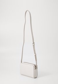 Obdélníková crossbody taška vyrobená z světle béžové kůže s hladkou texturou, nastavitelným popruhem a horním zipovým uzávěrem.